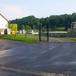 Blick auf die geöffnete Einfahrt zur Abwasseranlage in Leisnig. Links steht ein weißes Gebäude. Direkt hinter den offenen Toren ist eine Abwasserentsorgungseinrichtung sichtbar. Die Szene vermittelt einen Einblick in die kommunale Infrastruktur zur Abwasserbehandlung.
