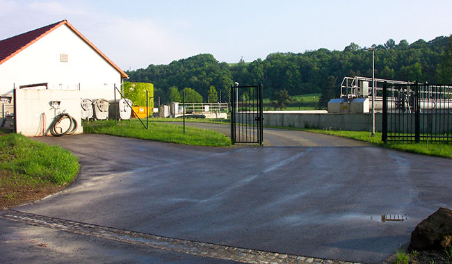 Blick auf die geöffnete Einfahrt zur Abwasseranlage in Leisnig. Links steht ein weißes Gebäude. Direkt hinter den offenen Toren ist eine Abwasserentsorgungseinrichtung sichtbar. Die Szene vermittelt einen Einblick in die kommunale Infrastruktur zur Abwasserbehandlung.